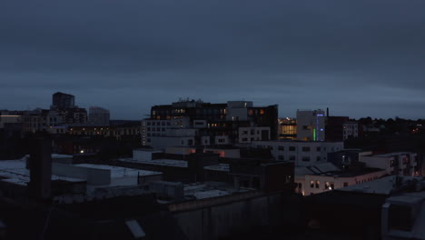 Forwards-fly-above-town-development.-Revealing-of-illuminated-bridge-over-Shannon-river.-Evening-city-after-sunset.-Limerick,-Ireland