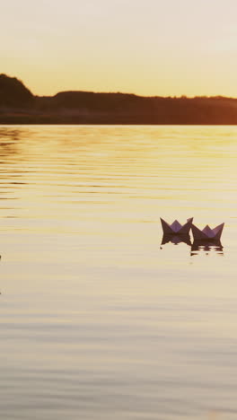 six origami in the form of boats sail by the lake at sunset in the evening. paper boats are drifting with the flow of water far away. vertical video