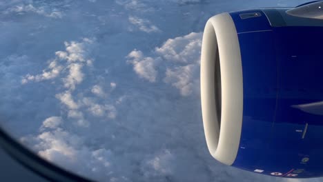 close up view of jet engine or turbine through glass window of an airplane flying over fluffy clouds in the sky