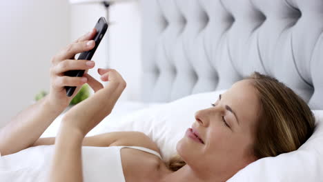 beautiful woman using phone in bed managing smart connected home with mobile app