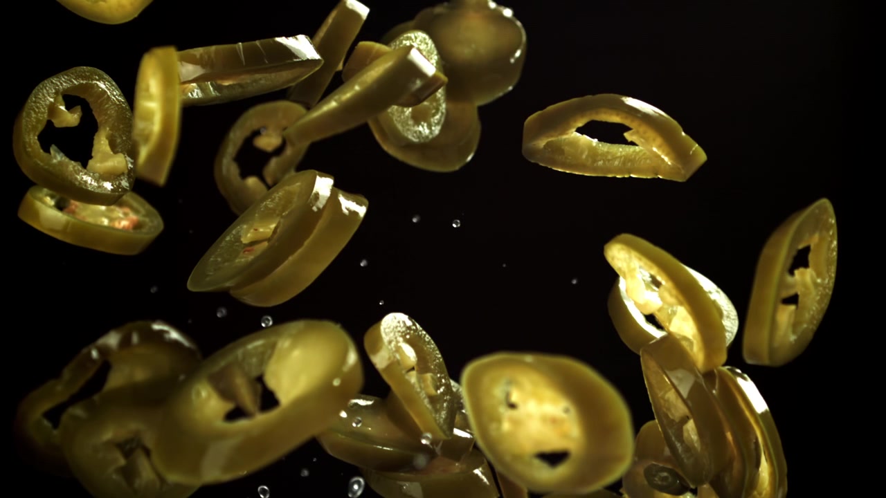 Jalapeños sottaceto a fette in caduta al rallentatore su sfondo nero.