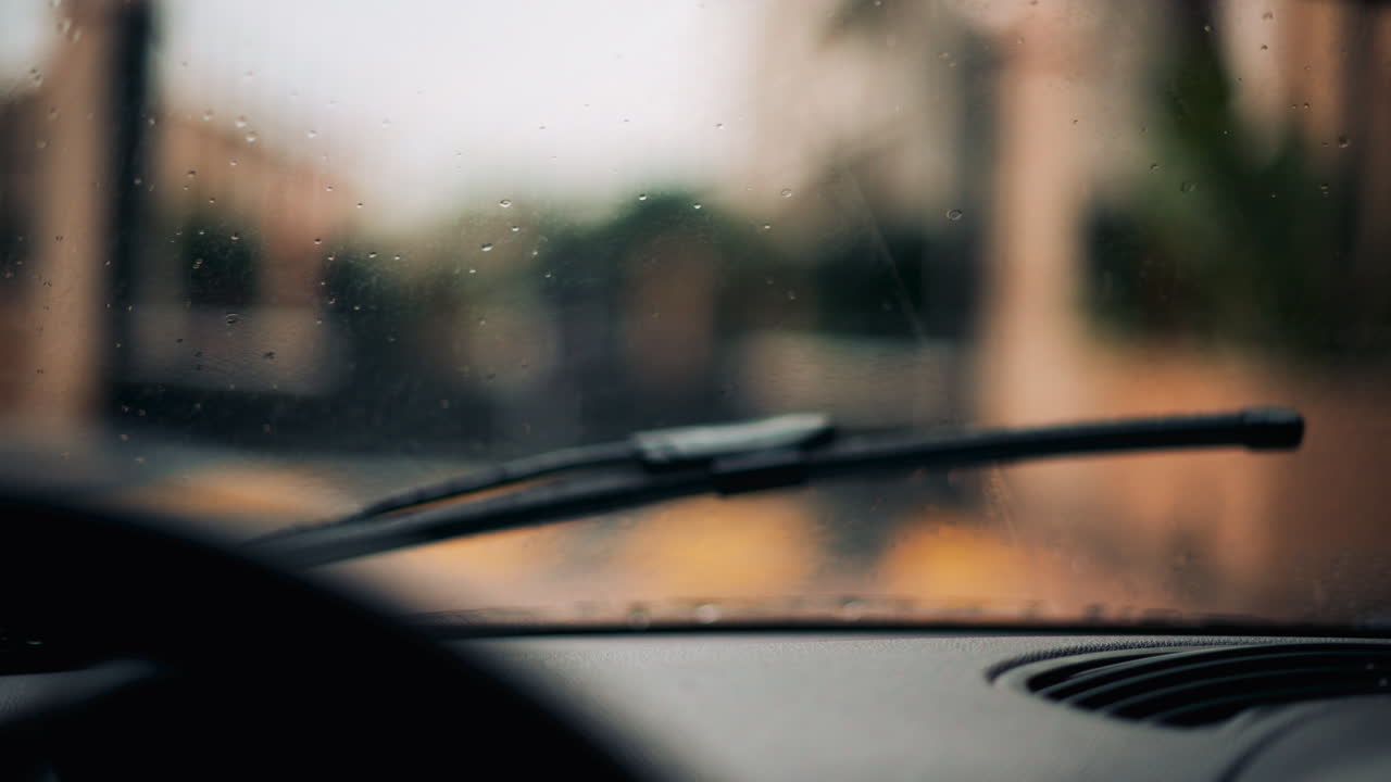 View from inside a car driving in the rain, wiping the drops off the windshield