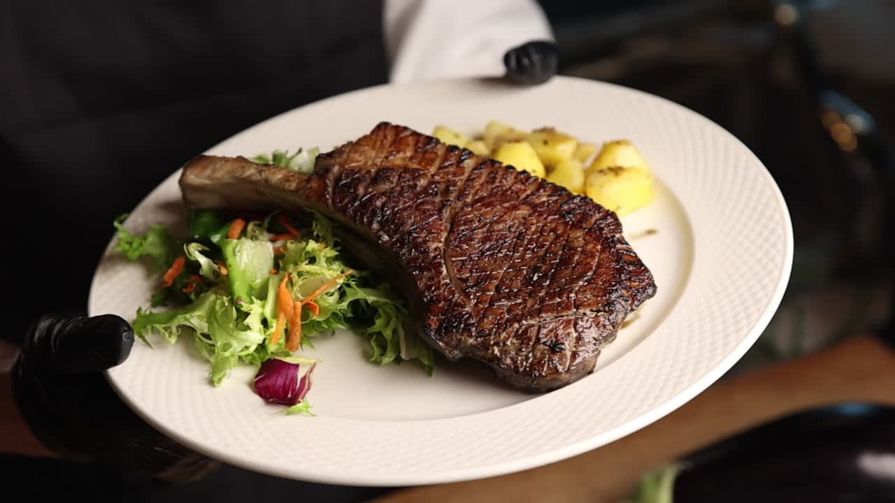 Chef che presenta una bistecca Tomahawk alla griglia con contorni