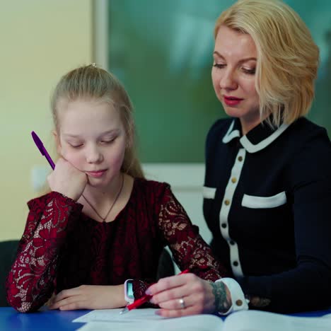 teacher and a schoolgirl in the classroom. female tutor teaches the little girl. elementary school teacher giving a student one to one support in the room.