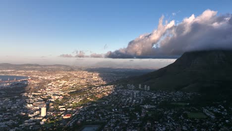 amazing aerial shot of town at sunset next to table mountain with clouds hanging overhead, shadows and warm light creating a dramatic look, cape town south africa