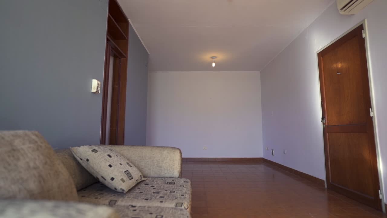 Slow right sliding clip showing cozy, modern airbnb apartment living room, with beige couch, white walls, and wooden floor and doors.