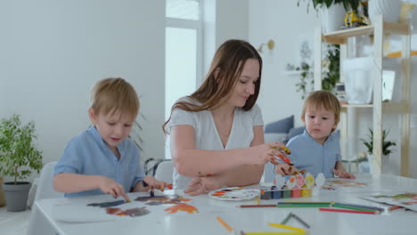 the family has fun painting on paper with their fingers in paint. mom and two children paint with fingers on paper