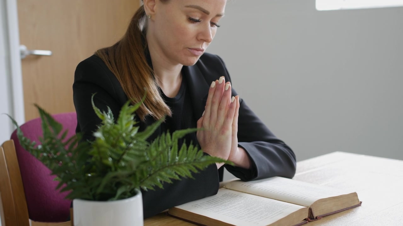 Preghiera. Una donna con le mani giunte mentre prega e legge una Bibbia.