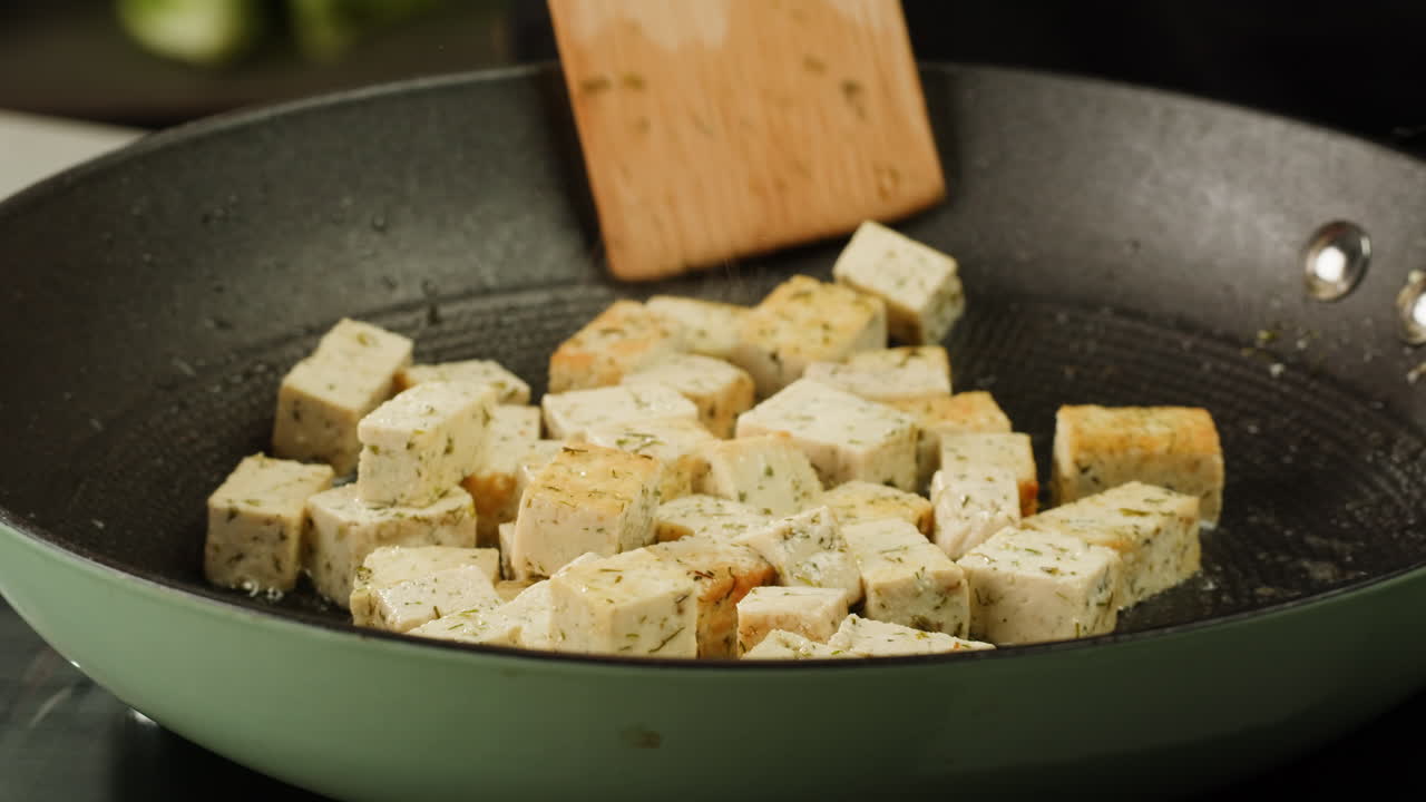 Fried tofu with sesame seeds and spices on cast iron pan, cooking japanese salad. Healthy ingredient for cooking vegan vegetarian diet food. Roasted tofu over black background.