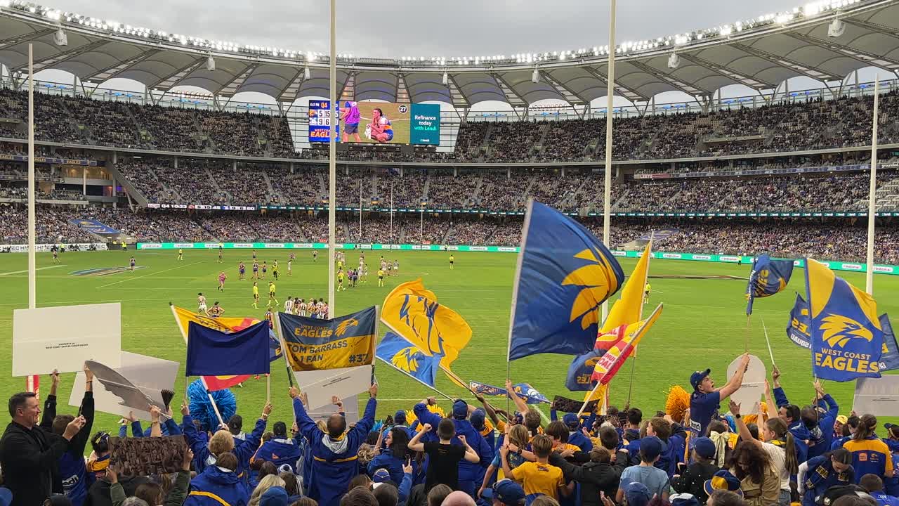 Australian Rules Football game at a crowded stadium with cheering fans and team flags