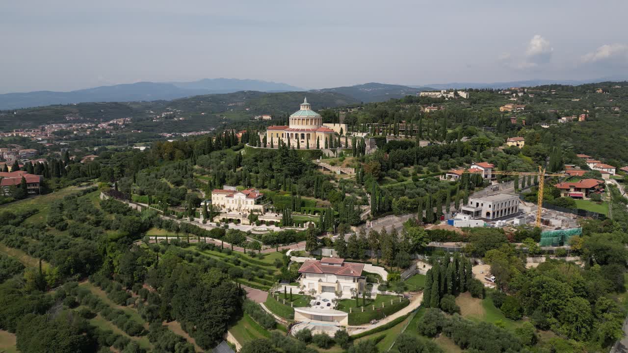vista aérea de una aldea de montaña muestra un gran edificio con un techo abovedado y una estructura circular en la cima de la colina rodeada de árboles verdes exuberantes más edificios y montañas se extienden hacia el horizonte