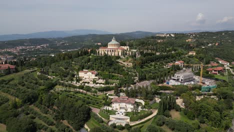 aerial view of a mountain village shows a large building with a domed roof and circular structure on top of the hill surrounded by lush green trees more buildings and mountains stretch out horizon