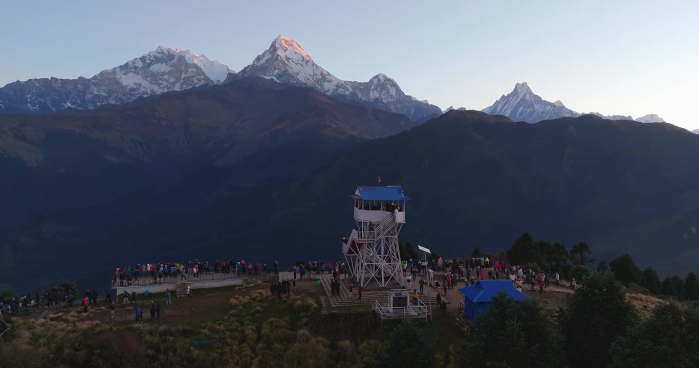 Annapurna Region, Poon Hill, Nepal, drone orbits around the iconic view tower and observation area filled with tourists taking in the panoramic sunrise view of the Annapurna mountain range.