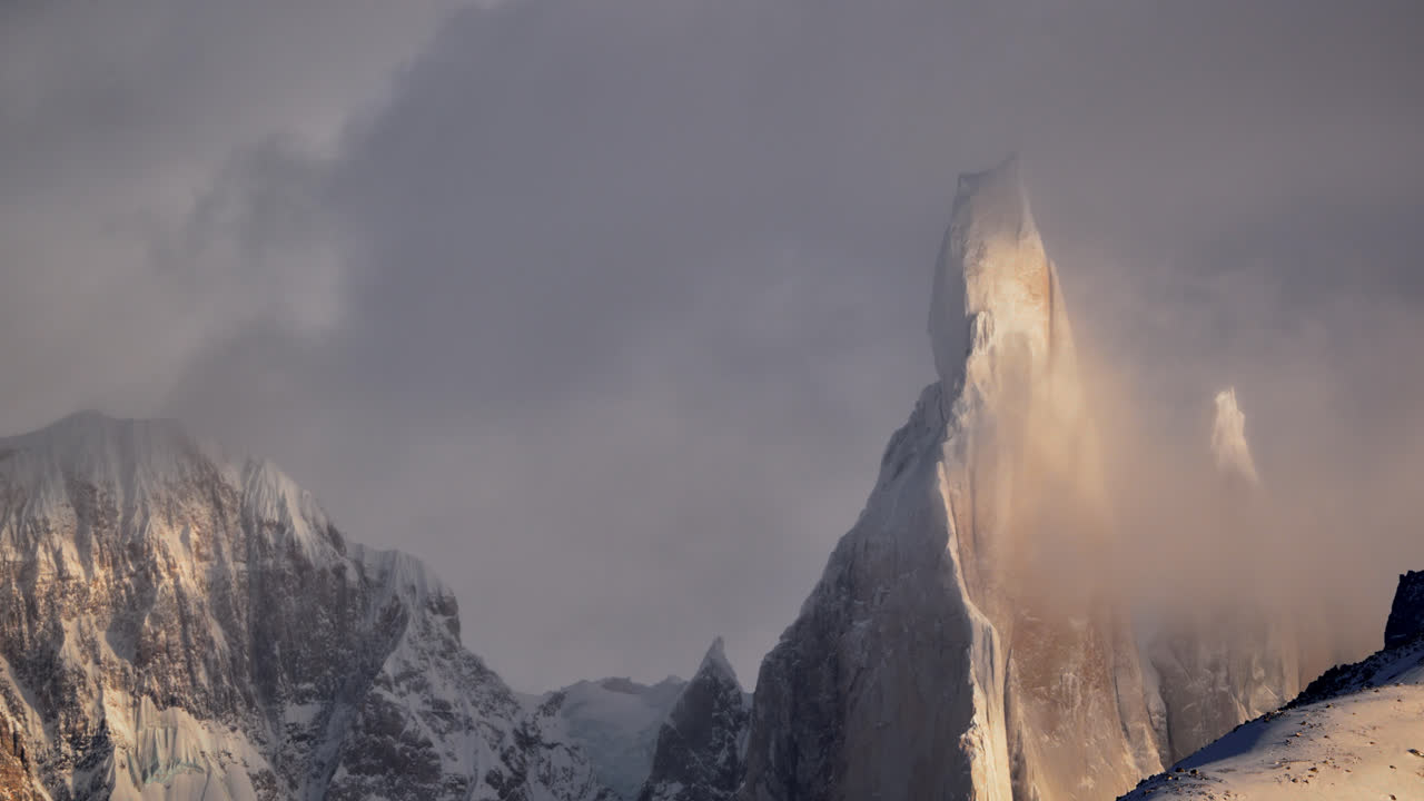 Sunset light hits Cerro Torre snowy peak as clouds swirl in a dramatic timelapse scene
