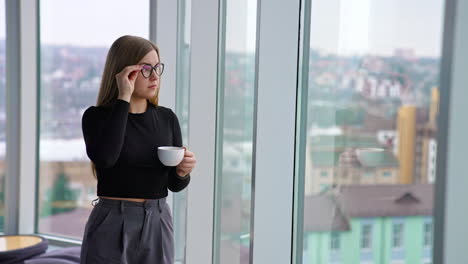 Beautiful female with cup of coffee standing by the window
