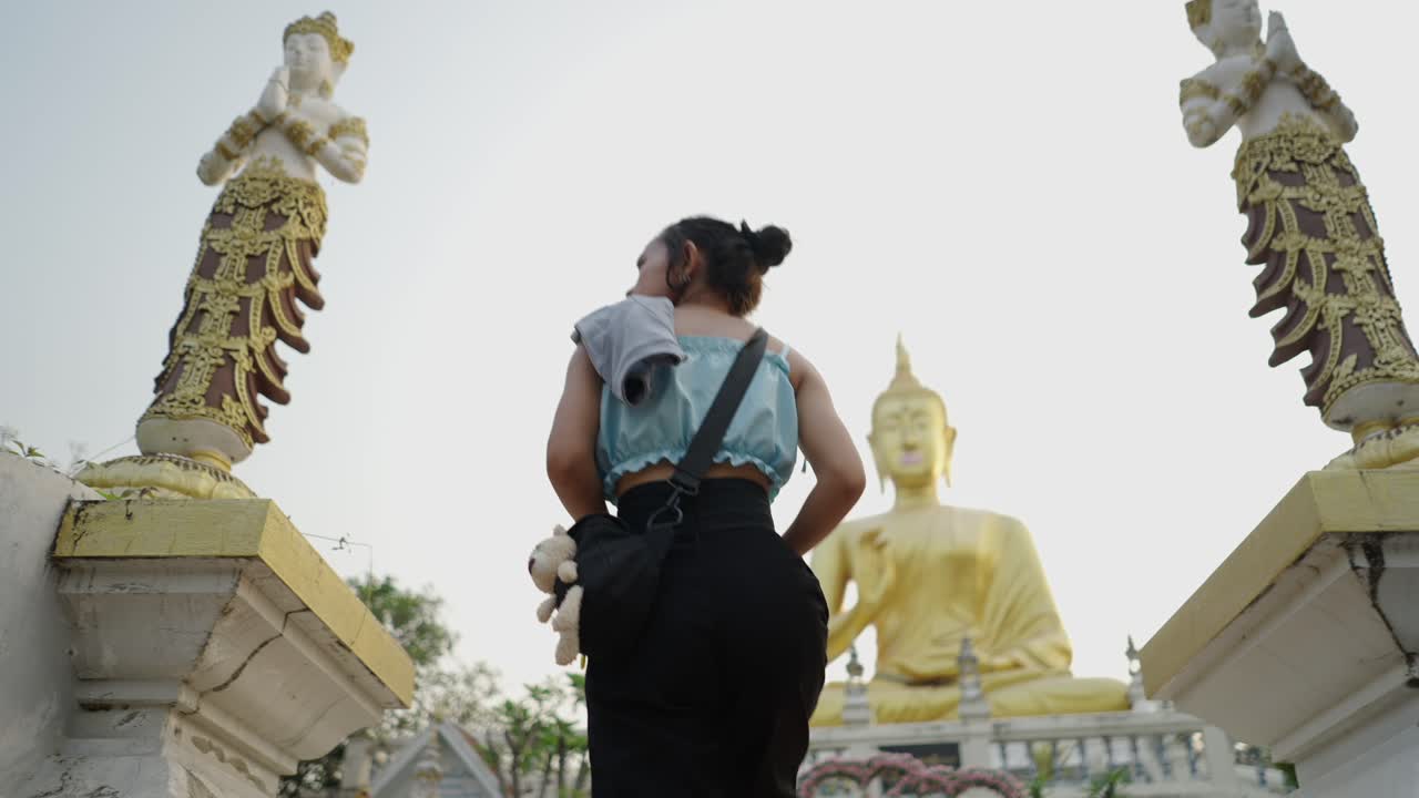 Woman approaches a large golden Buddha statue at a temple