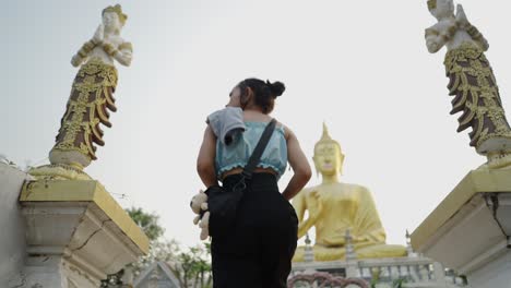 woman approaches a large golden buddha statue at a temple