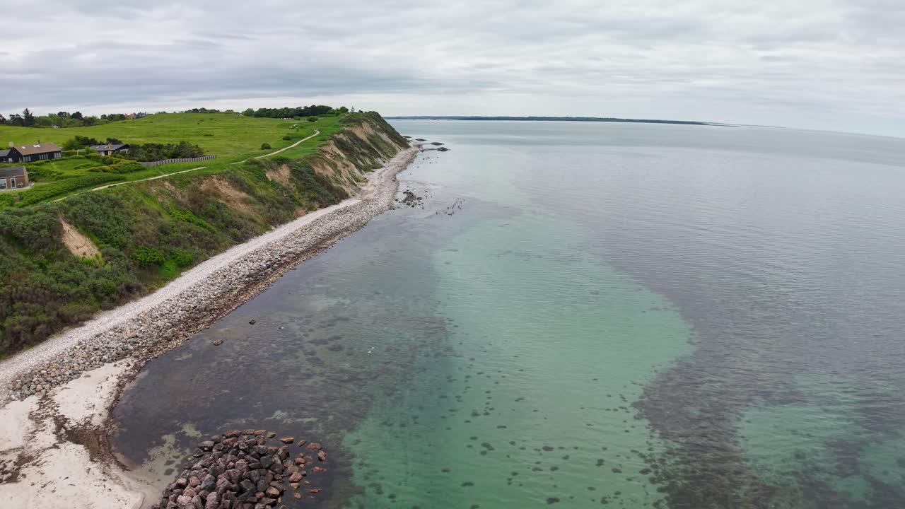 Aerial drone view of a rocky coastline with white sandy beaches, green cliffs, and clear turquoise water along the shore