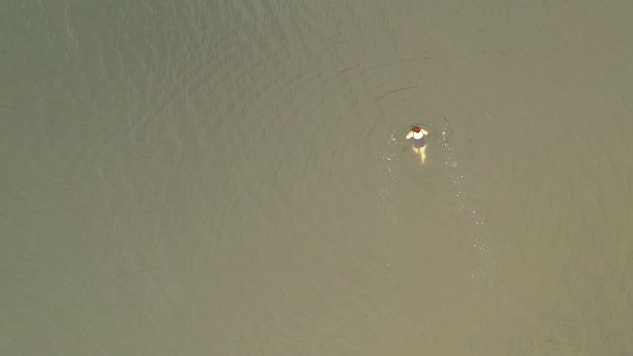 una vista de arriba hacia abajo de una mujer nadando en un traje de baño azul nadando sola en un arroyo verde