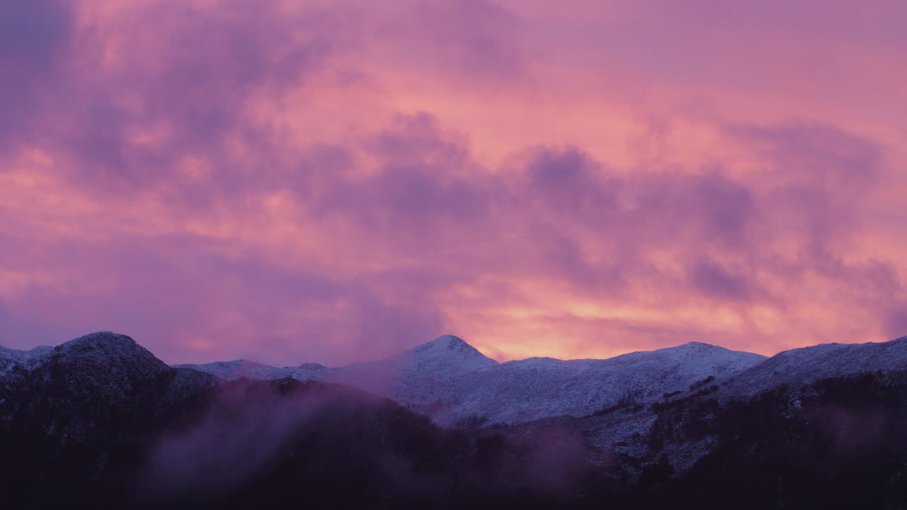 Scatto panoramico di montagne con un tramonto rosa sullo sfondo in Norvegia