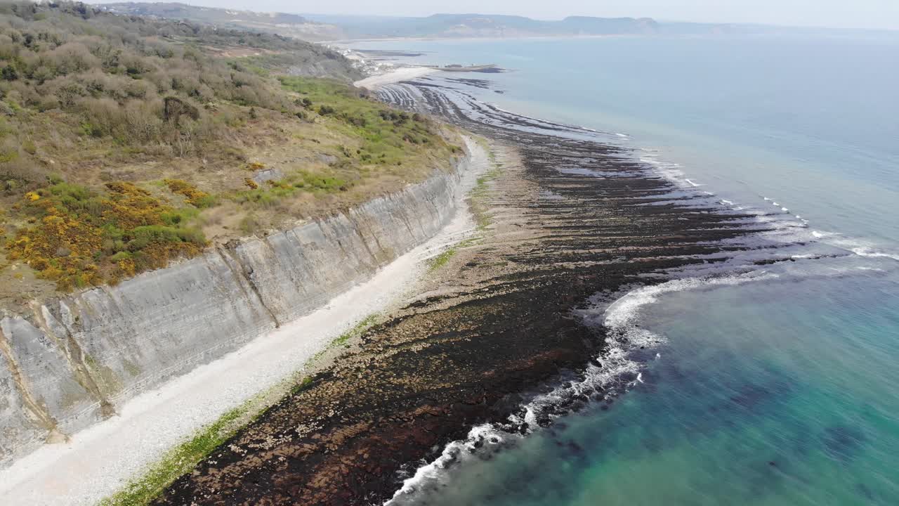 Coastal cliffs overlooking a serene beach and pristine waters on a sunny day. Aerial Circle Dolly Shot