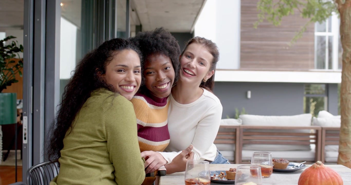 Amigas diversas rindo, se abraçando após conversa e sobremesas em mesa de pátio coberto