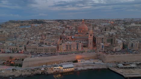 Una-Vista-Aérea-De-La-Antigua-Ciudad-De-La-Valeta-En-Malta-Al-Anochecer,-Cuando-Comienza-A-Iluminarse-Por-La-Noche.