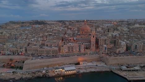 una vista aérea de la antigua ciudad de valletta en malta al anochecer, cuando comienza a iluminarse para la noche