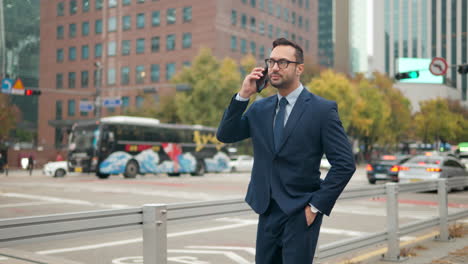 happy businessman talking on phone standing by office building, reporting good news