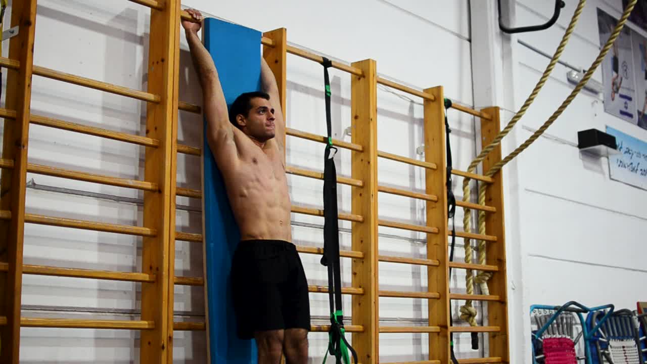 un tipo en un gimnasio de gimnasia haciendo levantamientos de piernas en una escalera y barras asimétricas todavía disparó una vista diagonal