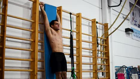 a guy in a gymnastics gym doing leg raises on a ladder and uneven bars still shot diagonal view