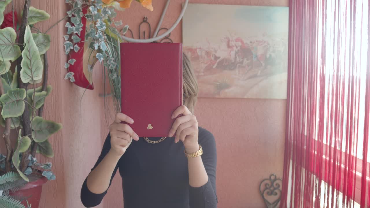 혀를 내밀고 얼굴을 드러내며 빨간 책으로 까꿍 놀이를 하는 매력적인 젊은 여성