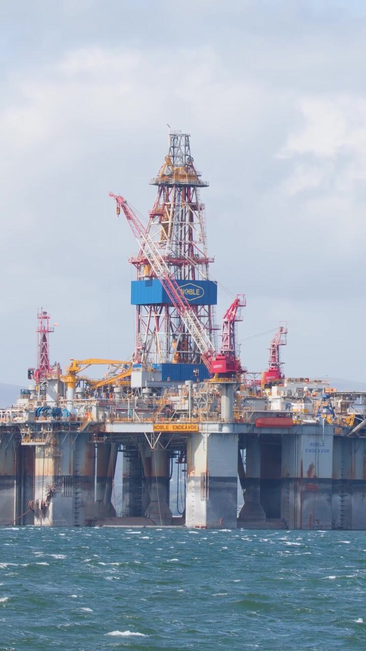 Large offshore oil rig platform in daylight, gentle camera pan, choppy sea, Scottish Highlands background