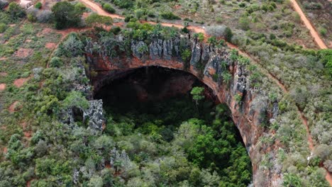 Aerial-drone-rotating-shot-of-the-large-Lapa-Doce-cave-entrance-of-colorful-rocks-with-a-self-contained-rainforest-below-in-the-Chapada-Diamantina-National-Park-in-Bahia,-northeastern-Brazil