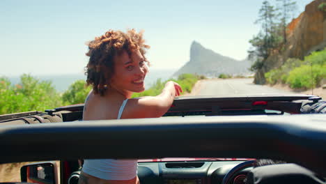 portrait of woman standing up through sun roof of car on road trip with friends through countryside
