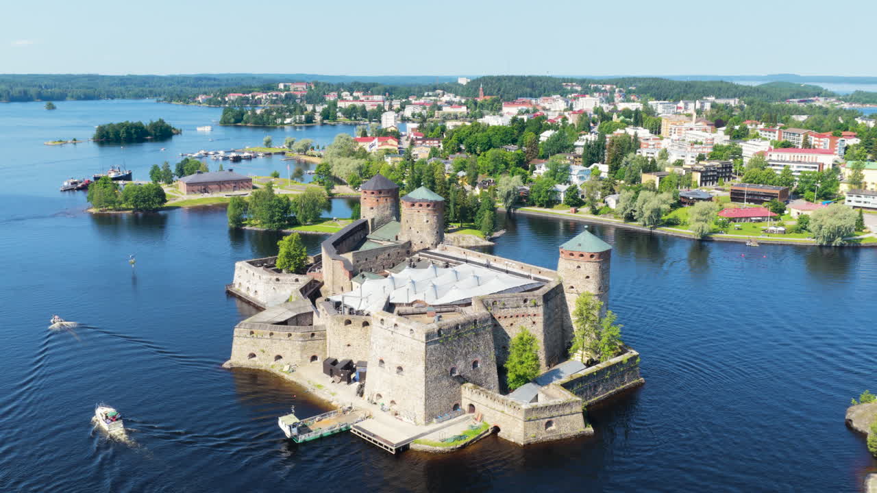 Drone flying around the Olavinlinna castle while boats move past it, in Finland