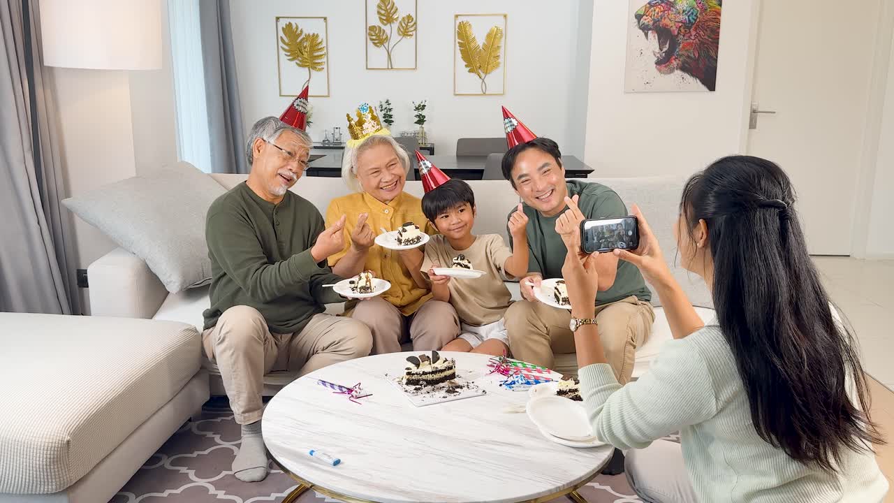 Three generations enjoy birthday cake together in a brightly lit living room, smiling for photos