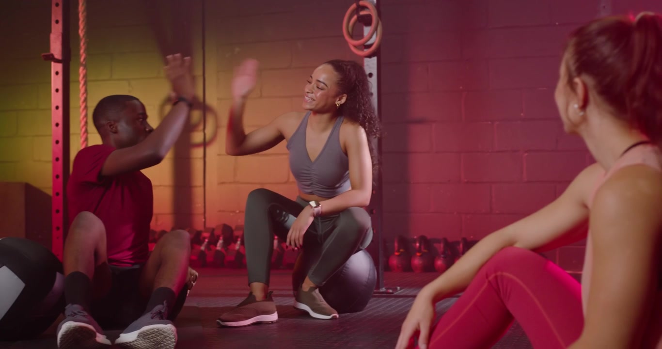 Diverse friends in sportswear chatting, sharing high-fives after workout at gym on stability ball