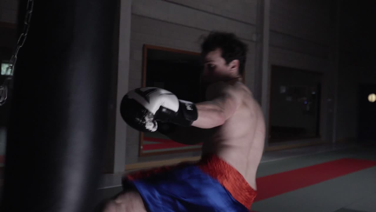 빈 체육관에서 무거운 가방을 때리는 공격적인 킥복서