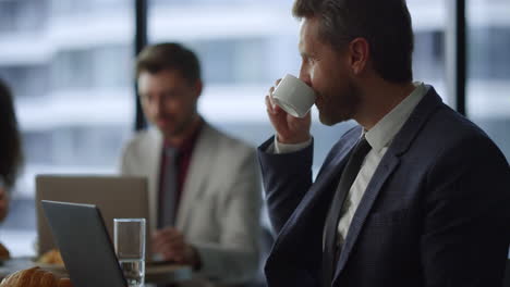 smiling executive man typing laptop device drinking coffee in coworking cafe.