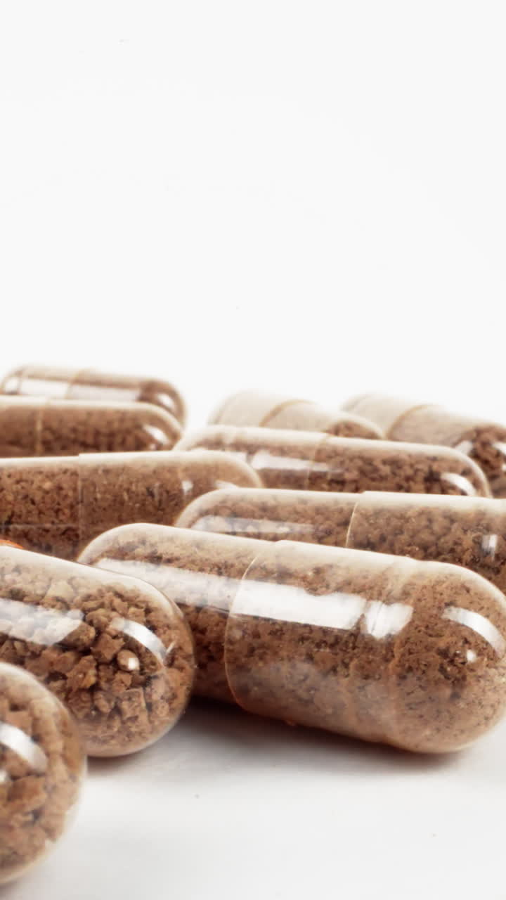 cápsulas múltiples transparentes llenas de polvo de hierbas marrón en una superficie blanca