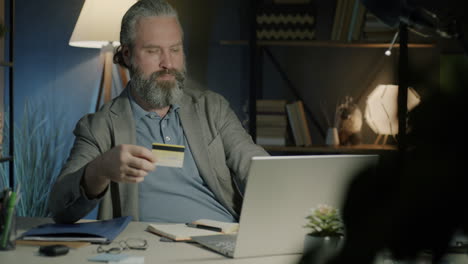 man using laptop and credit card at night