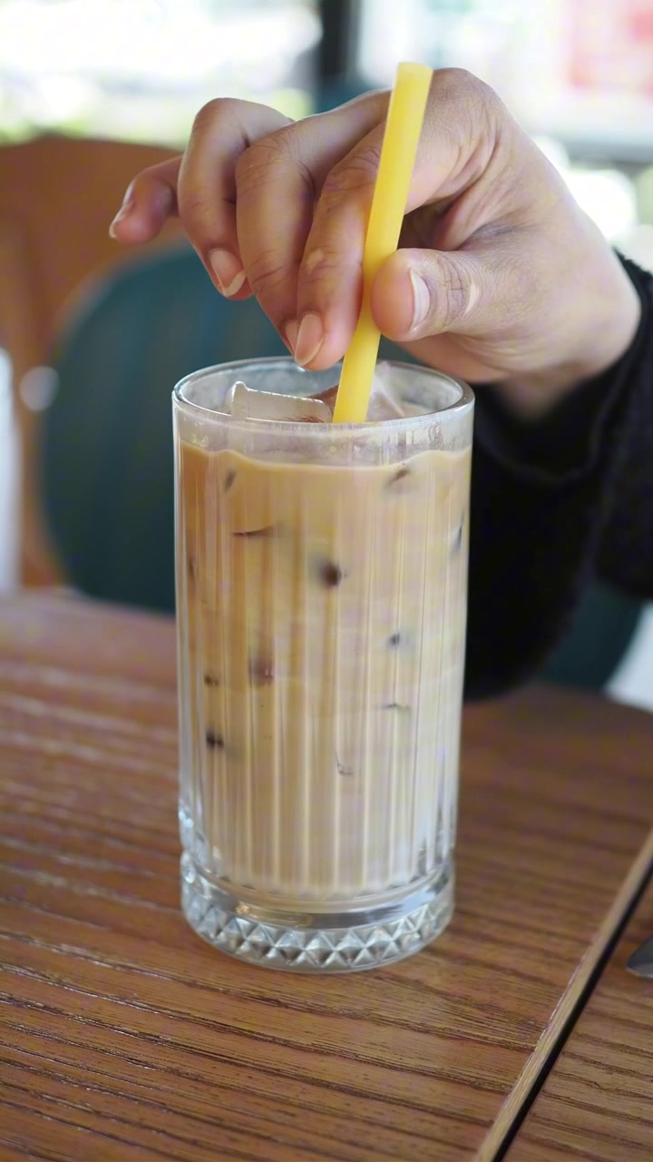 Persona che mescola caffè freddo con una cannuccia gialla in un bar