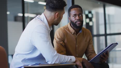 video of two diverse businessmen discussing document at office meeting