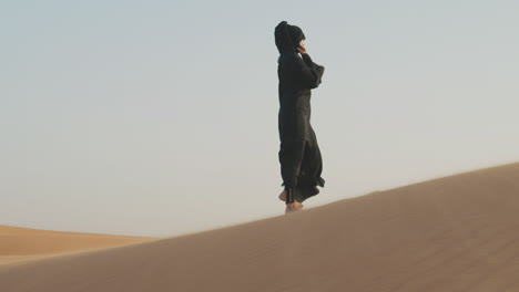 beautiful muslim woman in hijab walking barefoot in a windy desert 1