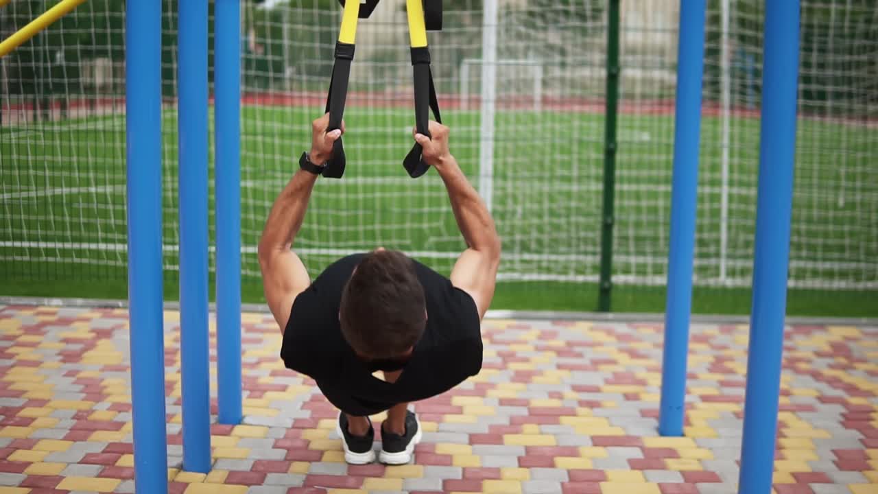 deportista caucásico haciendo ejercicios de pull ups usando cinturón de ajuste para forzar la fuerza del entrenamiento al aire libre
