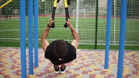 Deportista-Caucásico-Haciendo-Ejercicios-De-Dominadas-Usando-Un-Cinturón-De-Ajuste-Para-Forzar-La-Fuerza-Del-Entrenamiento-Al-Aire-Libre