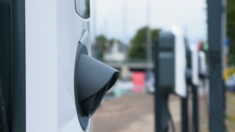 Sistema-De-Estación-De-Carga-De-Coches-Eléctricos-En-Una-Calle-De-La-Ciudad,-Futuro-Del-Automóvil,-Energía-Limpia-Y-Sostenible,-Día-Nublado,-Toma-De-Cierre,-Fondo-Desenfocado