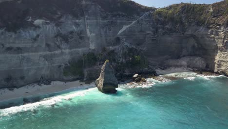 aerial view of the crystal blue water of diamond beach in nusa penida, indonesia with a prominent large cliff in the foreground