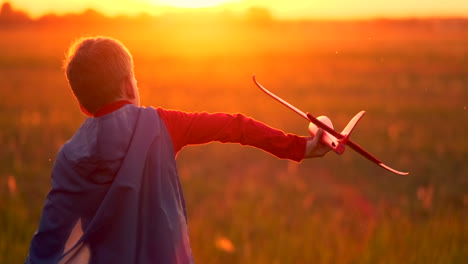 piloto de niño corre en un impermeable rojo sosteniendo un avión riendo al atardecer en el campo de verano imaginando que es un piloto de avión jugando con un modelo de avión